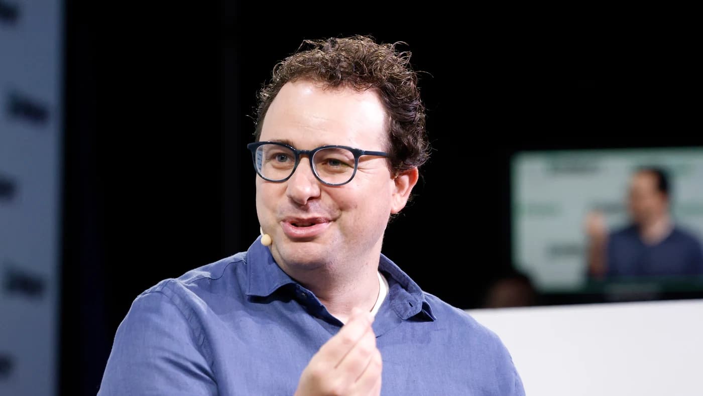 Dario Amodei in a blue shirt and glasses speaking on a conference stage
